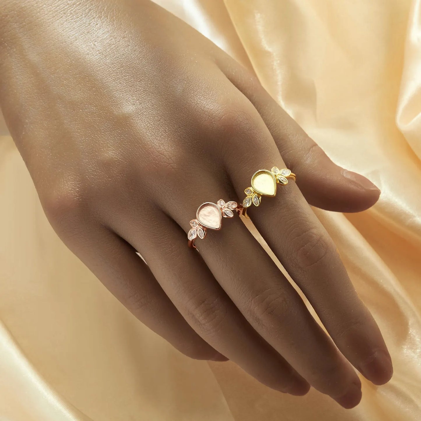 Hand wearing a gold ring with floral design on a soft peach fabric background