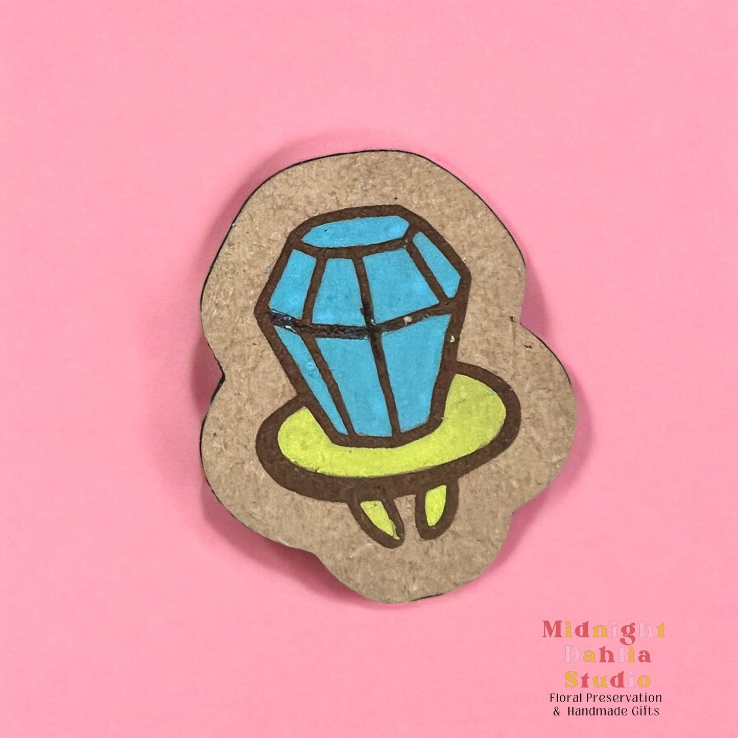 A wooden pin with a hand painted ring pop candy with blue candy and a lime green base. Retro and vintage vibes.