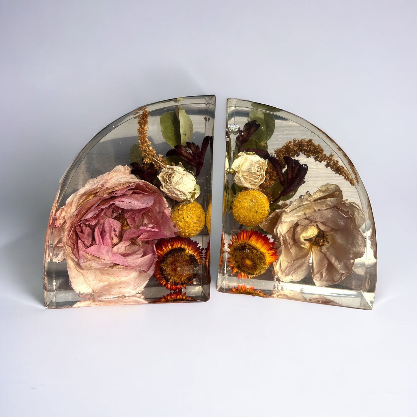 Custom resin bookend set made with white flowers included fall colors with orange and yellow strawflower , yellow billy balls craspedia , white spray mini roses , rust brown amaranthus , burgundy red kangaroo paw , and pink mauve roses. A flower preservation option that is useful home decor forever.