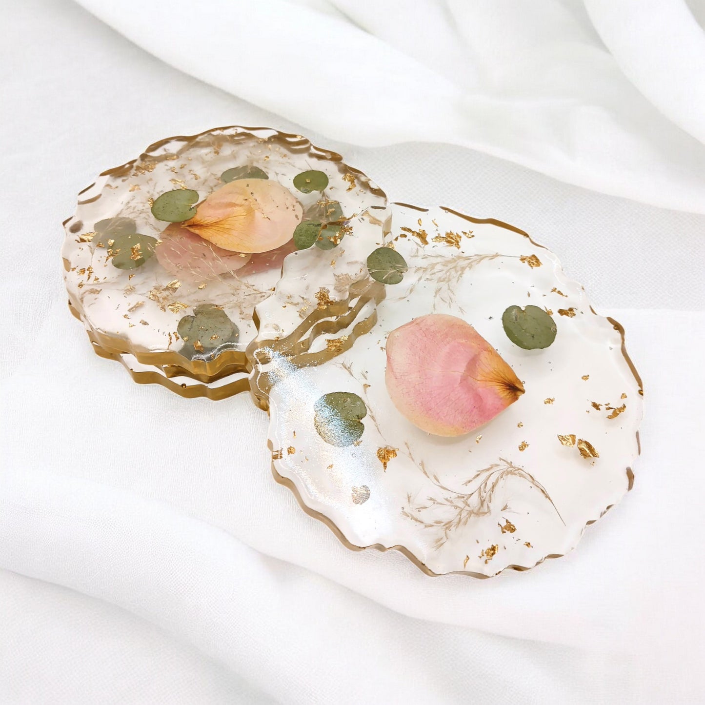 A custom resin coaster set with pink rose petals , green eucalyptus leaves , and gold flake with gold edges . A beautiful addition to a bridal bouquet preservation.
