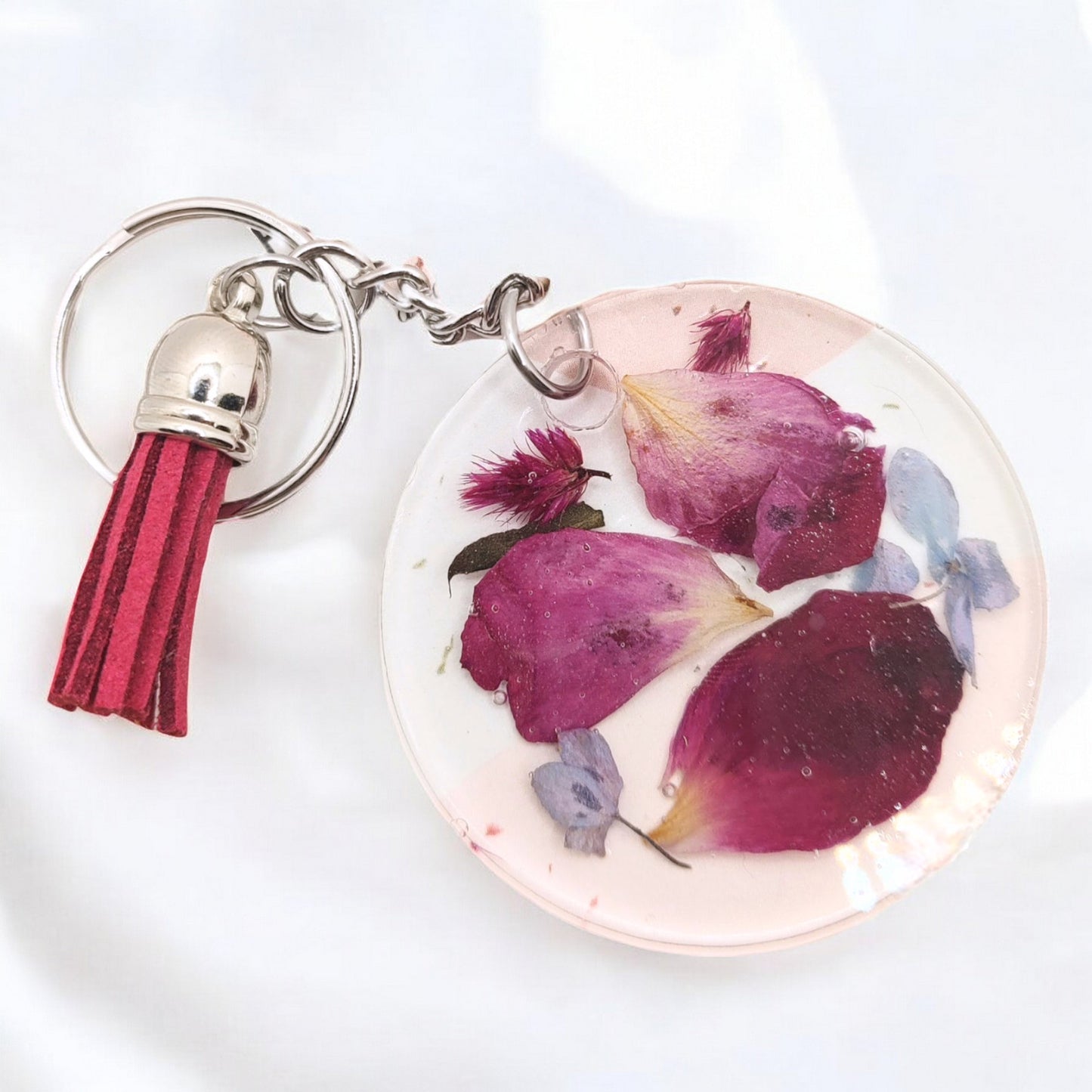 Custom crystal clear resin keychain filled with small red pink rose petals , blue tiny mini flowers , and small pieces of burgundy red celosia flower. A perfect addition to a bridal bouquet preservation.