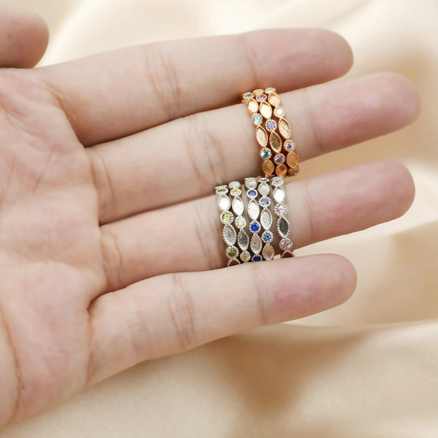 Three rings with gemstones on a hand against a beige background