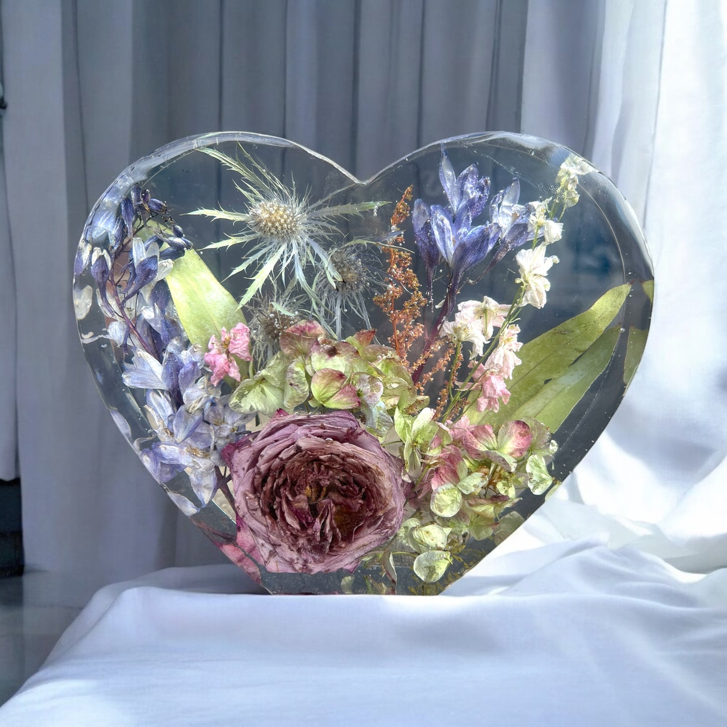A custom large heart set made with dried purple roses , purple and white hydrangea , blue delphinium , blue thistle , peach orange astilbe , and other flowers. Handmade with crystal clear resin and a beautiful way to preserve a bridal bouquet.