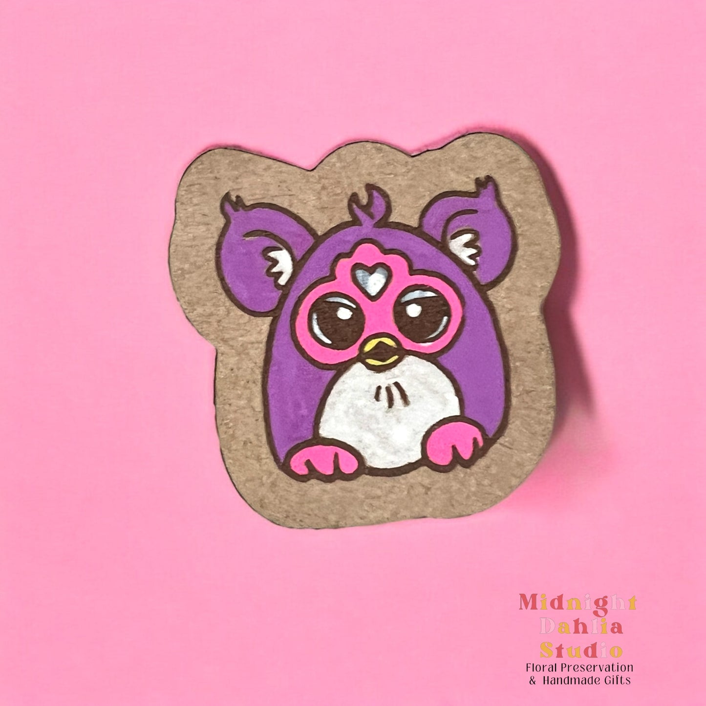 A wooden pin with a handpainted Furby toy animal that is purple and white with pink feet and face. Retro and vintage vibes.