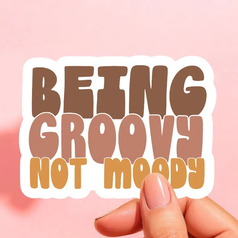 a sticker that reads being groovy not moody in brown, taupe, and orange yellow on a white background in a retro font