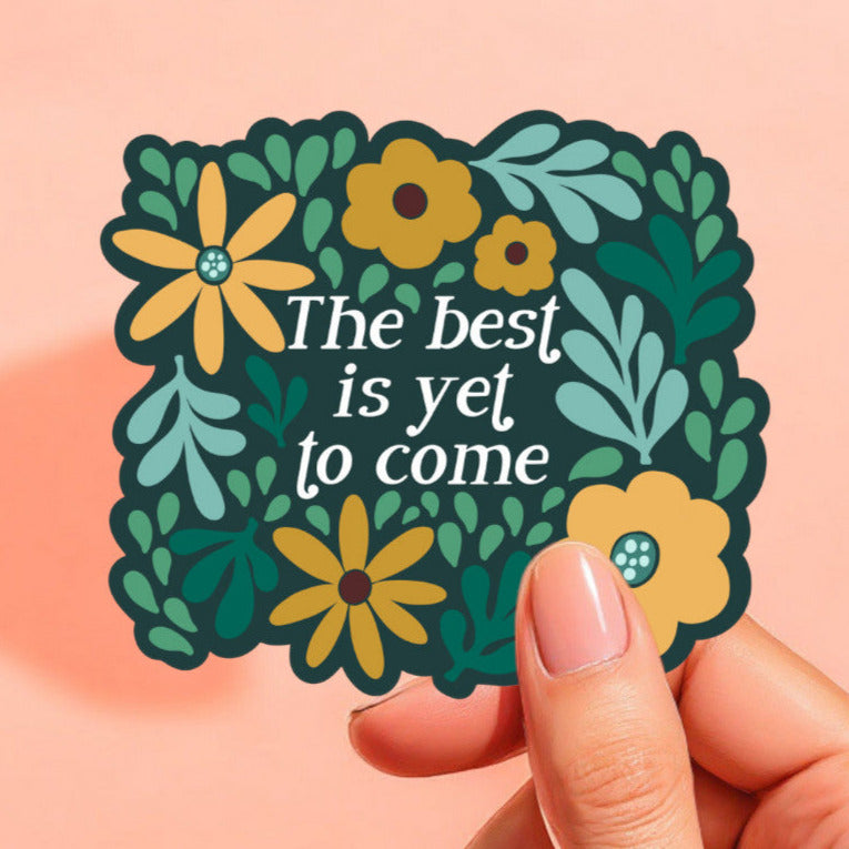 a green sticker that reads the best is yet to come surrounded by yellow, mint, green, and teal flowers