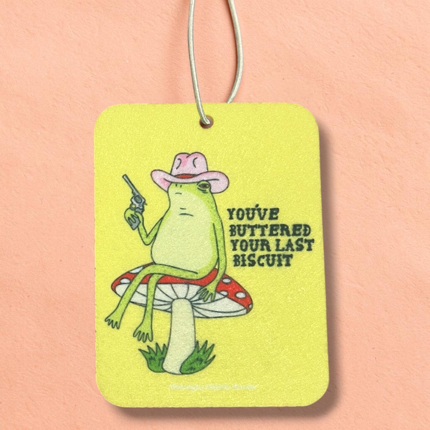 Frog character with a cowboy hat and gun on a yellow tag with text, against a pink background
