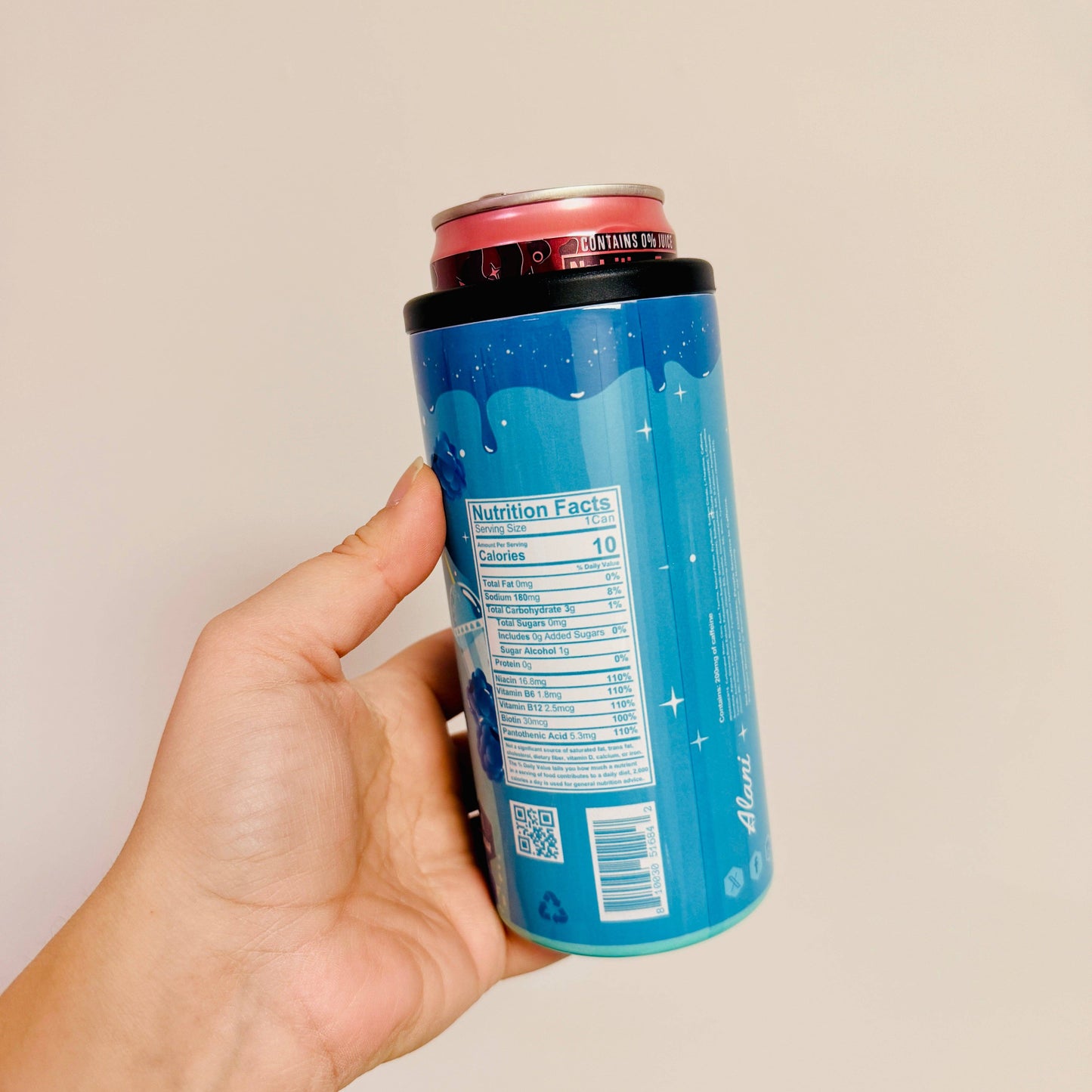 Hand holding a blue can with a red top against a beige background