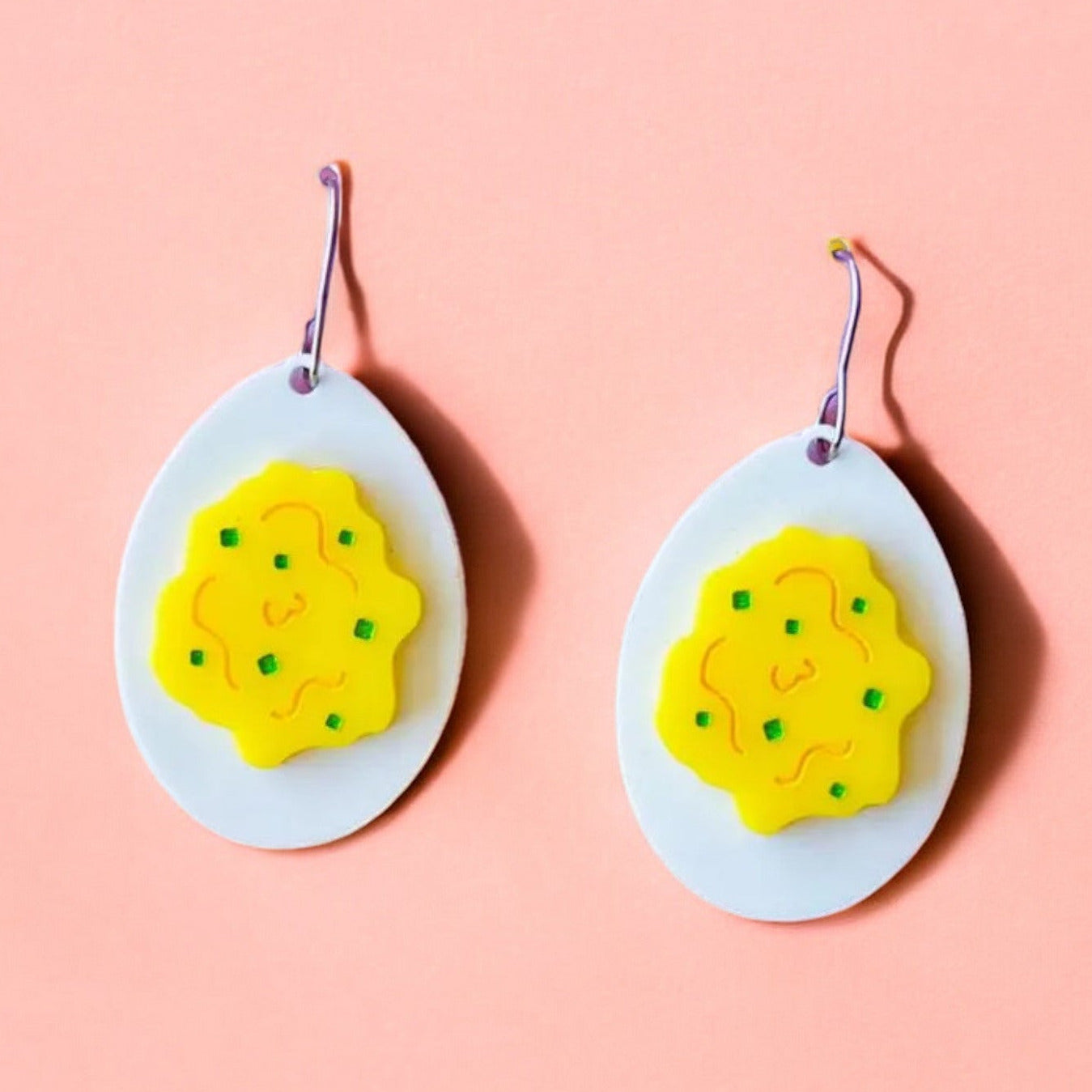 A pair of earrings shaped like eggs with a white acrylic background and yellow on top to make it look like a deviled egg. Perfect easter accessory.