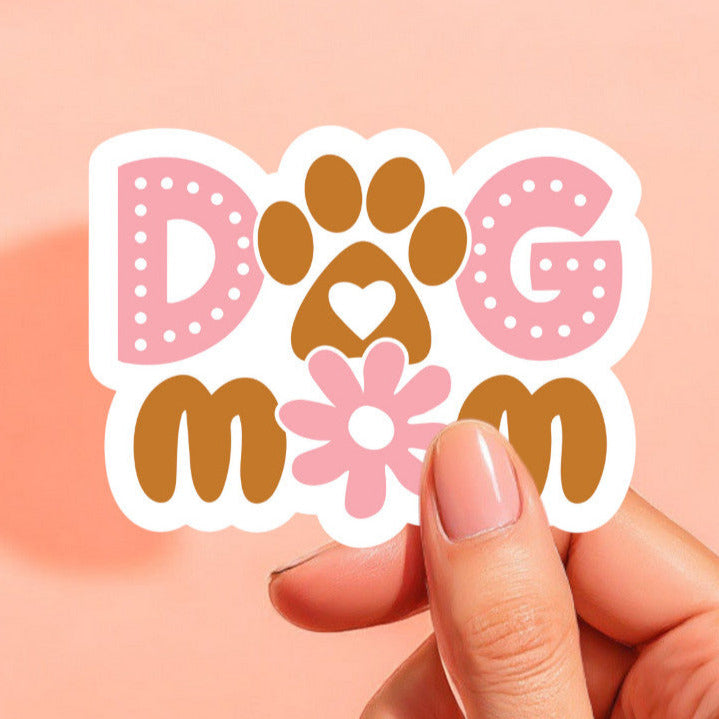 a white background sticker that reads dog mom with a paw print as the o in dog and a daisy as the o in mom. the sticker is printed in brown and pink.