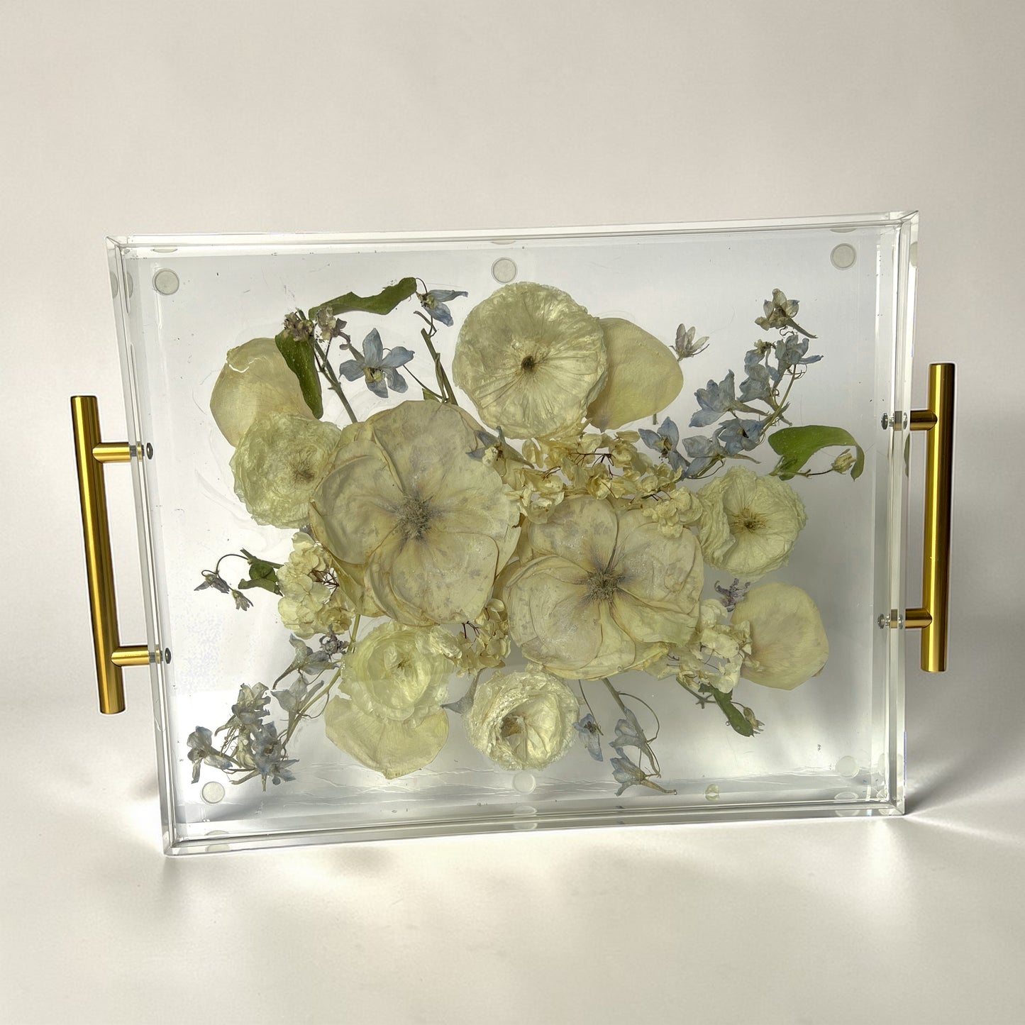 Decorative tray with pressed flowers and gold handles on a white background
