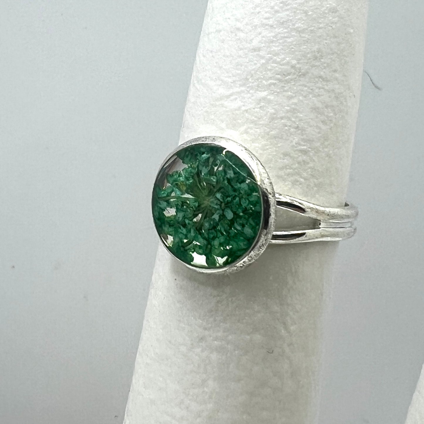 Silver ring with a green queen anne's lace flower on a white cylindrical stand.