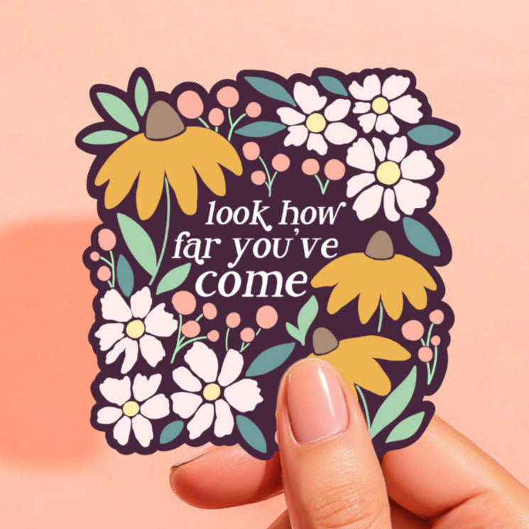 a sticker with a dark purple background that reads look how far you've come in white, surrounded by flowers