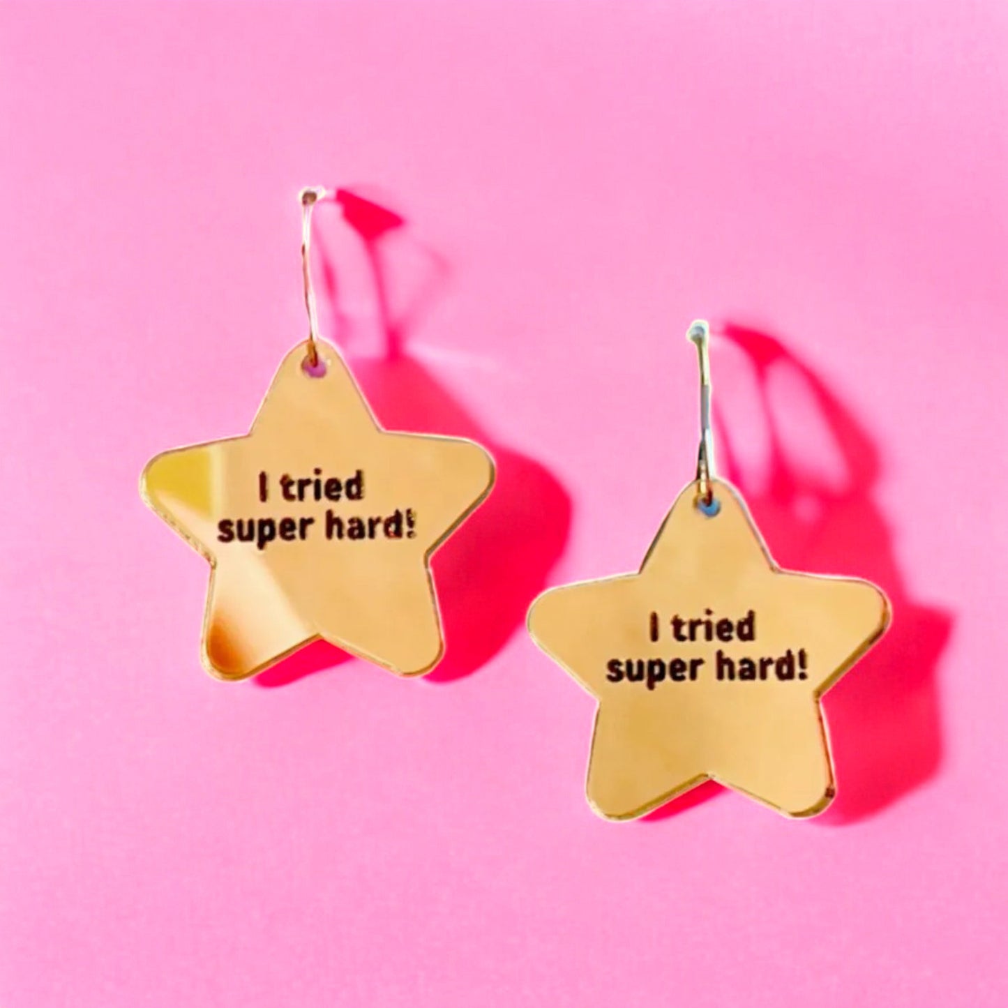 a gold star shaped pair of earrings that read i tried super hard! a perfect accessory for teachers or any woman women.