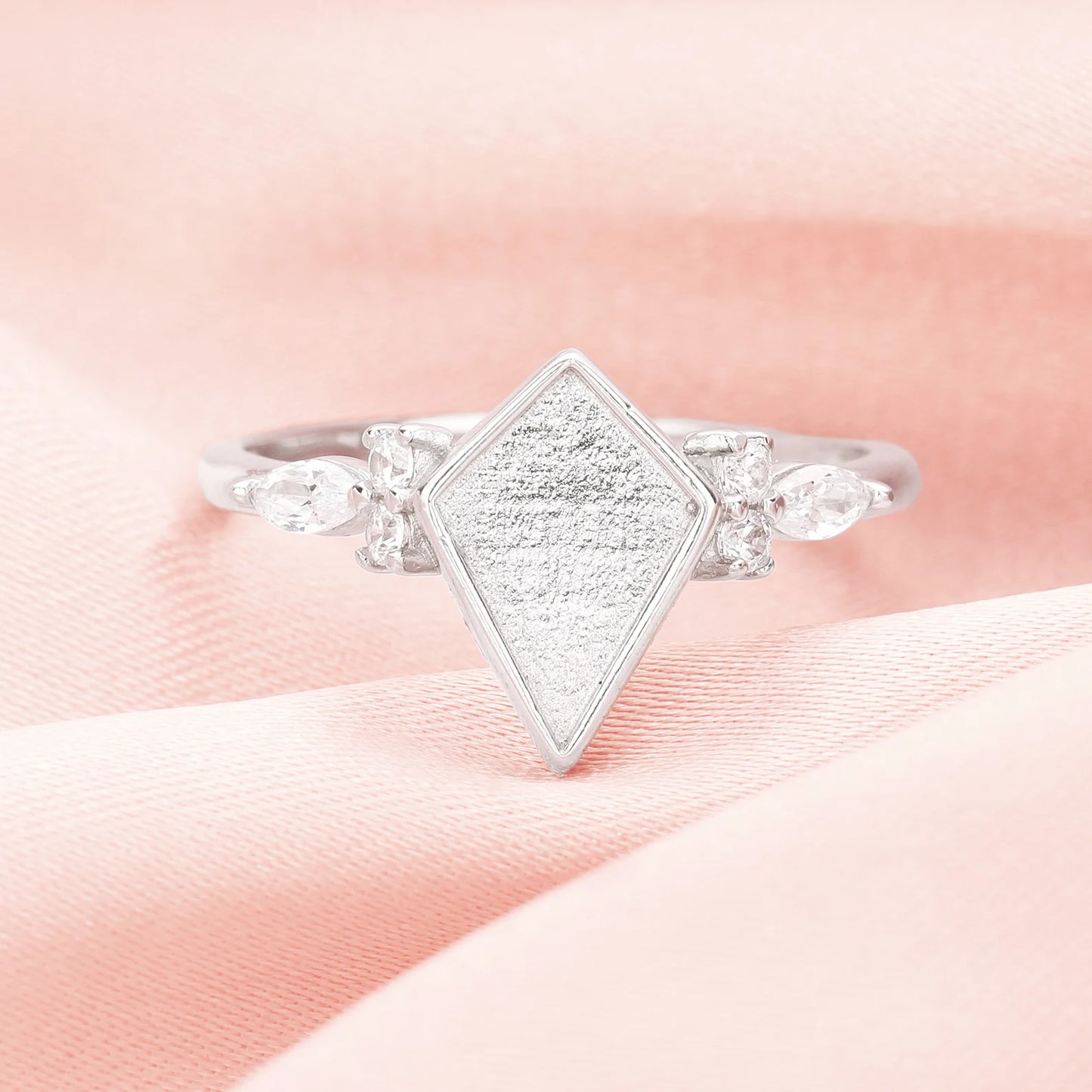 Silver ring with a textured diamond-shaped center on a pink fabric background