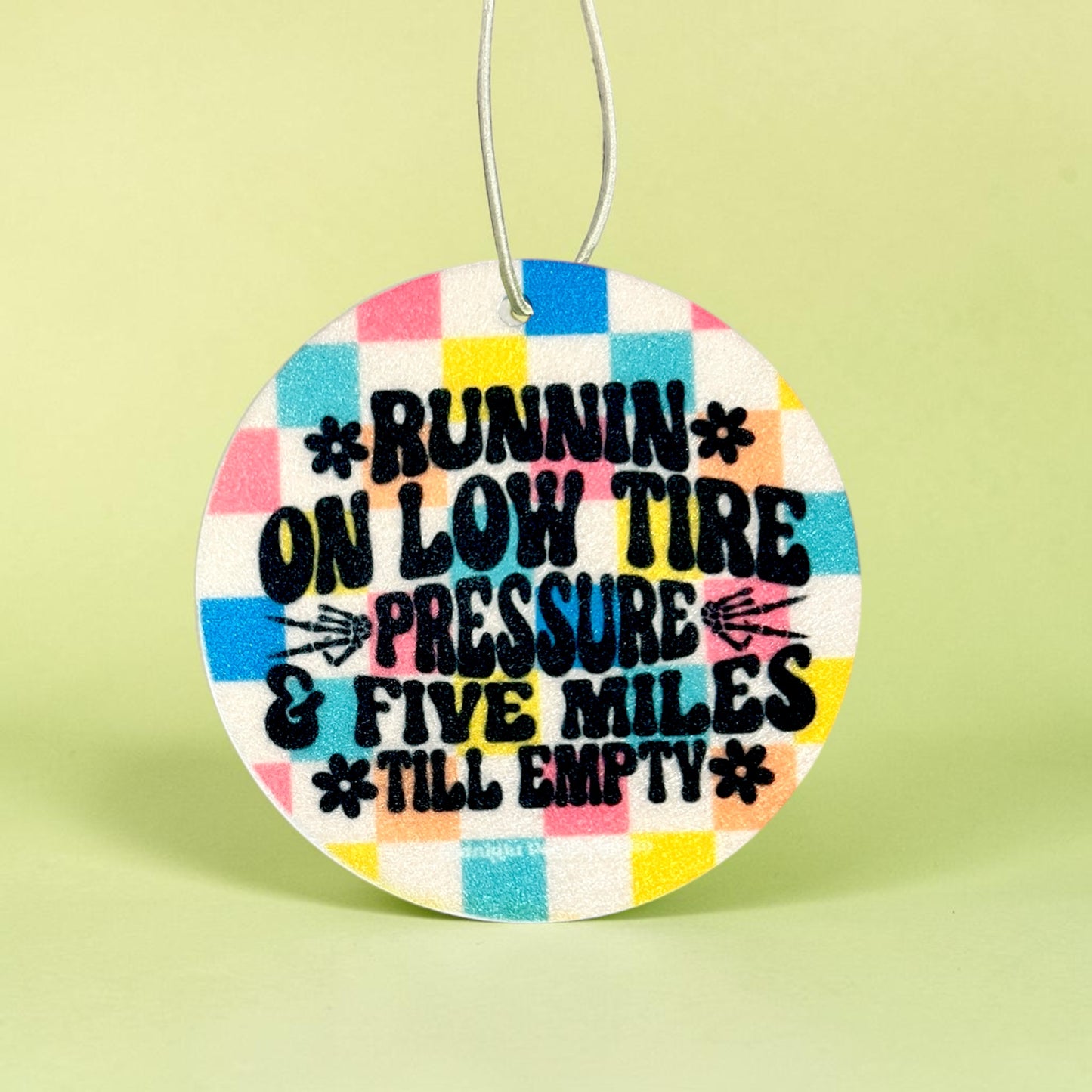 Round colorful car air freshener with humorous text on a light green background