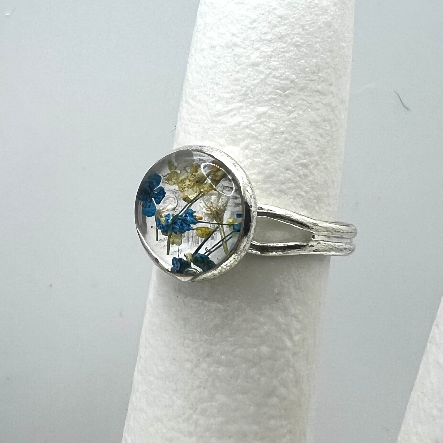 Silver ring with a circular design featuring blue and yellow flowers on a white background