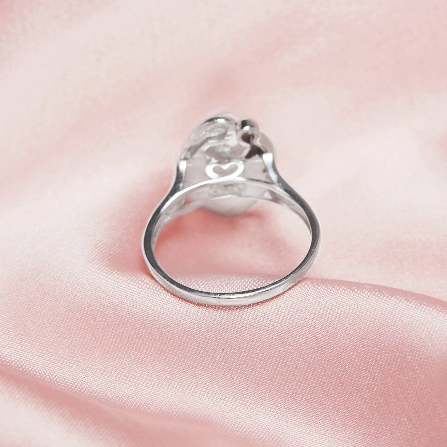 Silver ring with a heart design on a pink fabric background