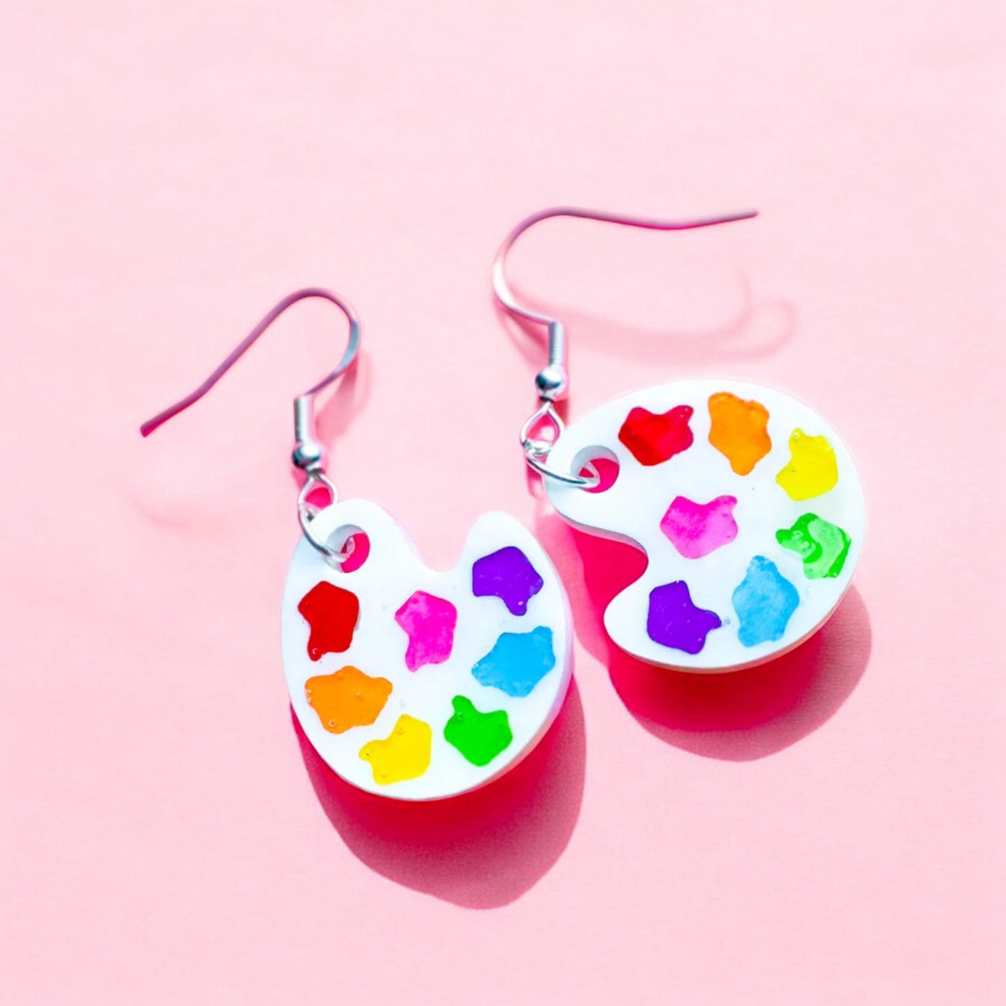 a paint palette shaped earring with multi colored blobs to resemble paint and a black tassel to look like a paint brush. a perfect gift for an artist or art teacher.