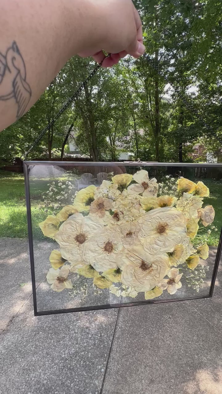A custom pressed flower floating frame with white roses , and green eucalyptus .   A beautiful way to preserve a bridal bouquet.