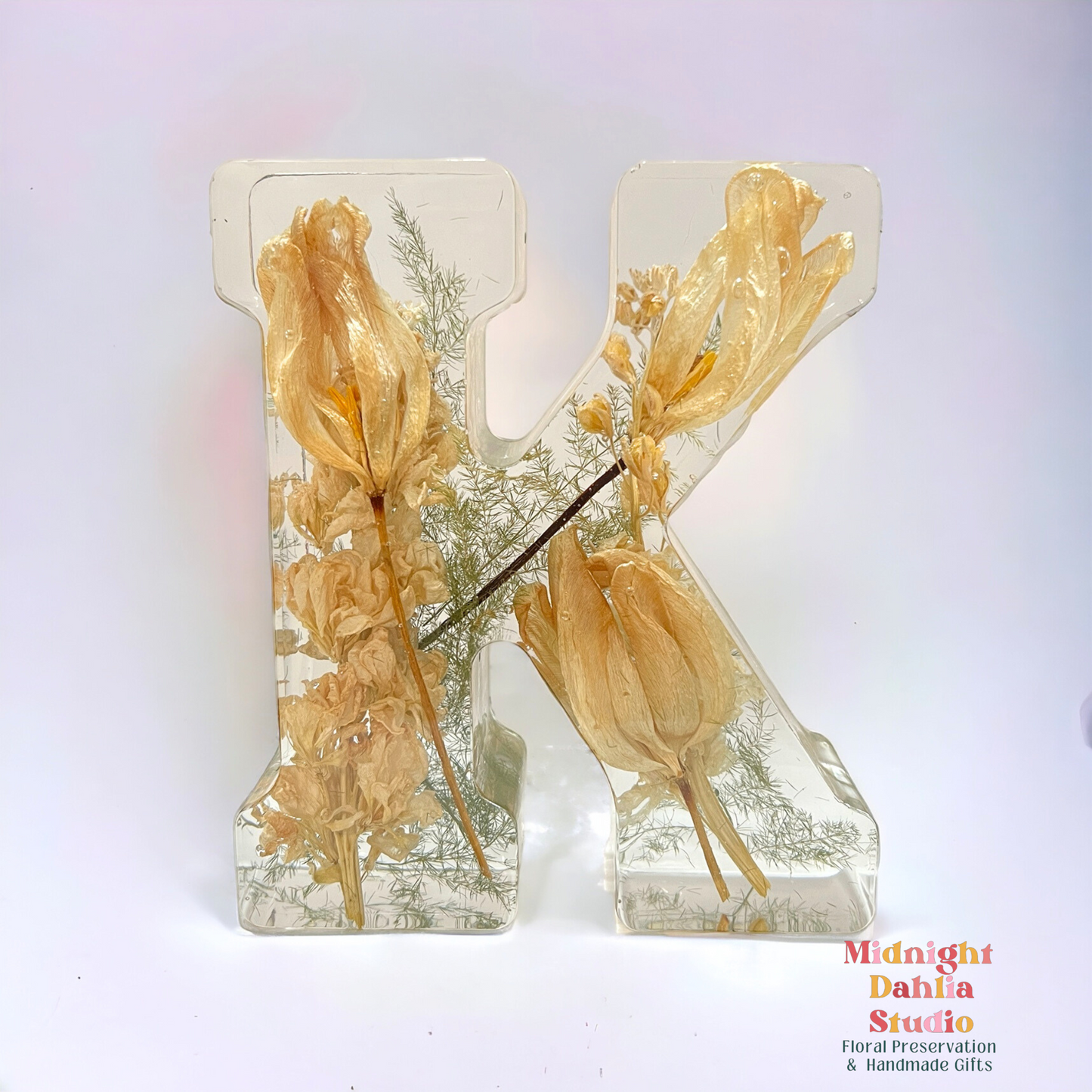 A crystal clear resin letter K with dried preserved flowers , including white tulips and white stock . A beautiful way to preserve your bridal bouquet.