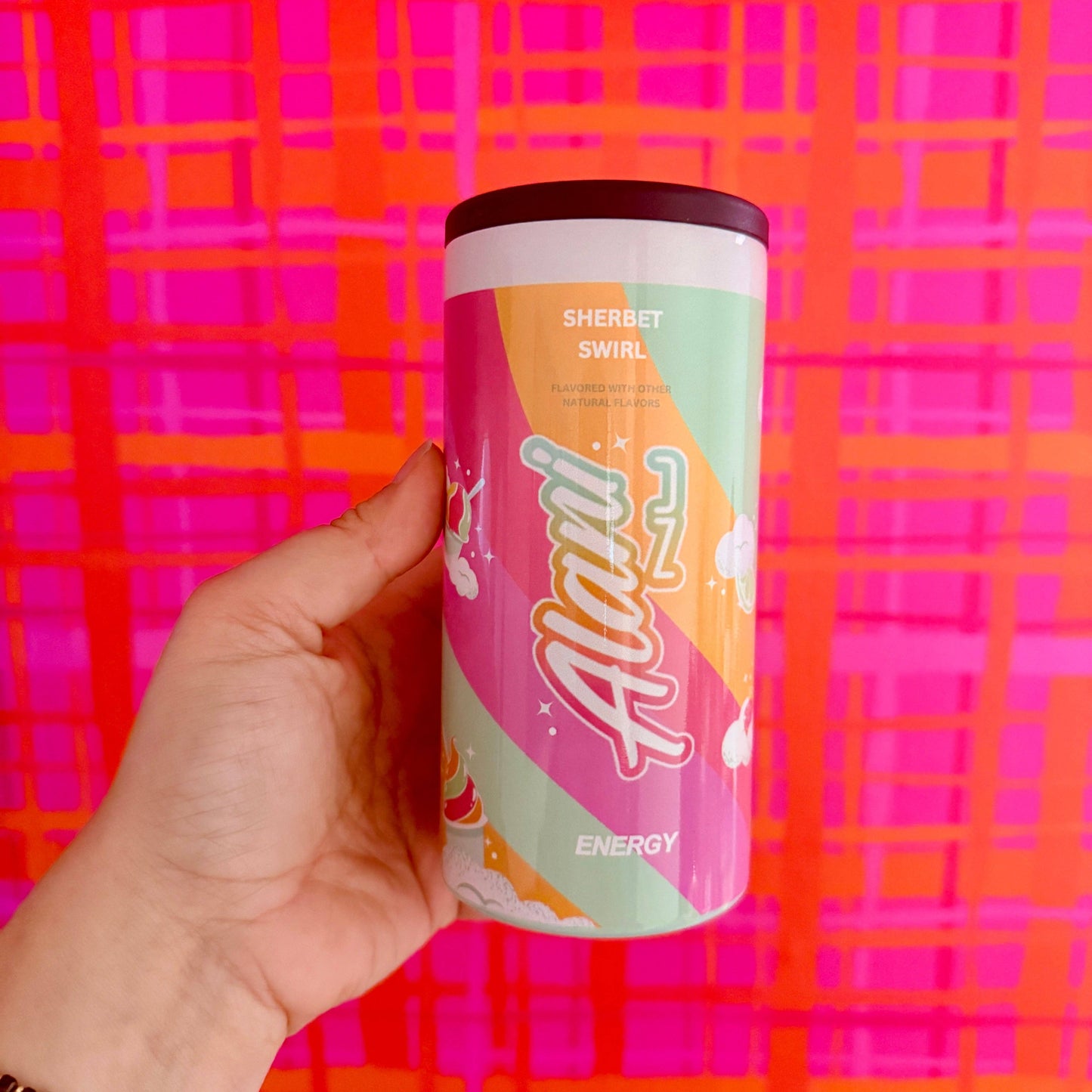 Hand holding a colorful energy drink can against a vibrant pink and orange plaid background