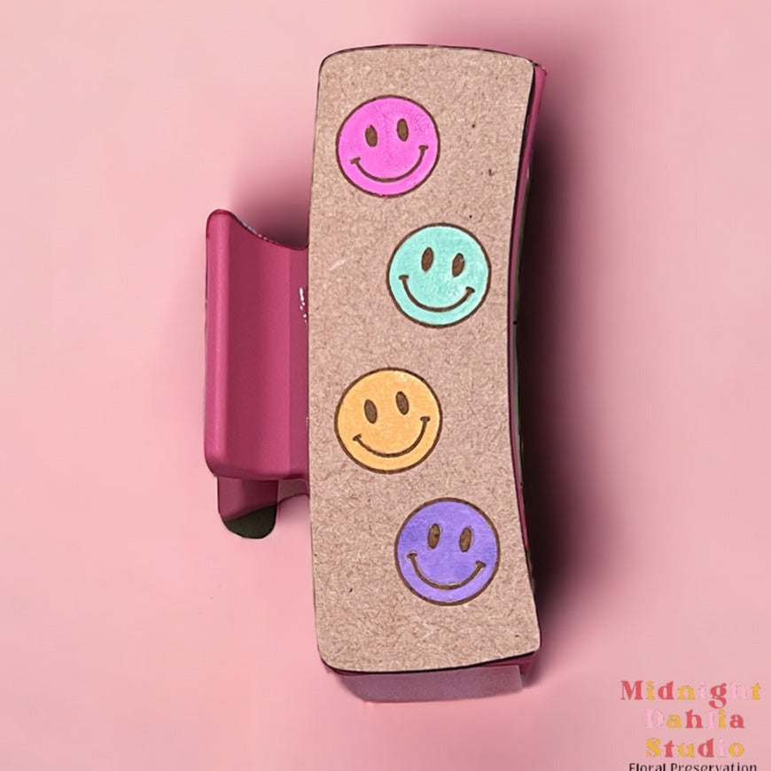 a claw hair clip with smiley faces in pink teal blue green yellow and purple
