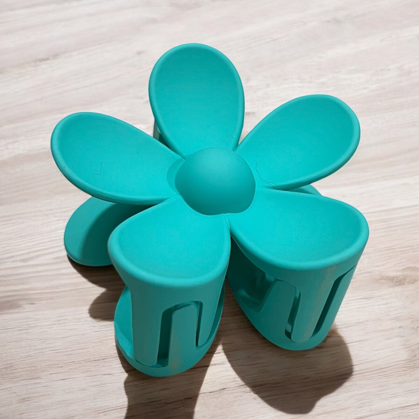a daisy shaped plastic claw hair clip in turquoise blue green