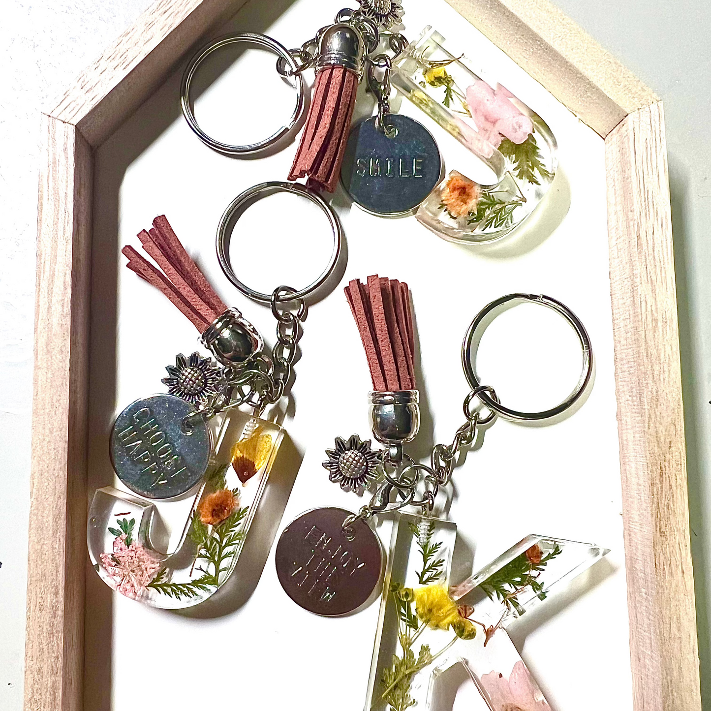 A custom resin letter keychain collection with tiny multicolor flowers. The keychain has gold hardware and an off-white tassel. It is a beautiful addition to a bridal bouquet preservation.