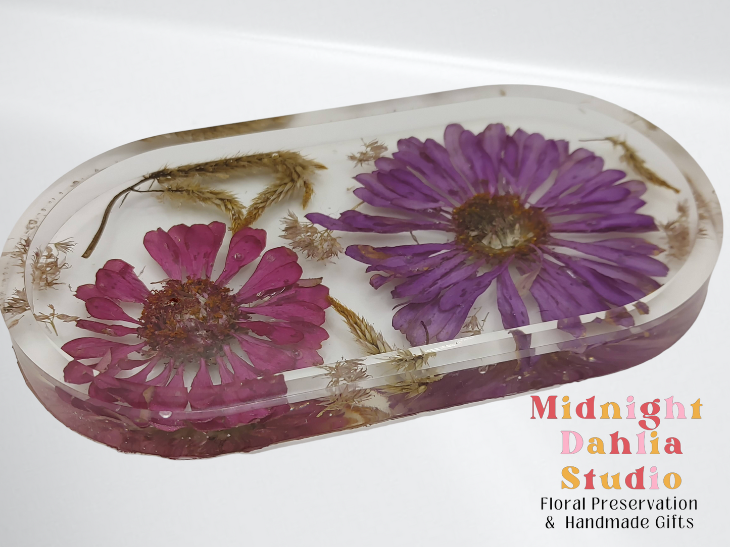 A custom vanity tray filled with dried pressed flowers including pink and purple zinnia . It is made of crystal clear resin with a white base.
