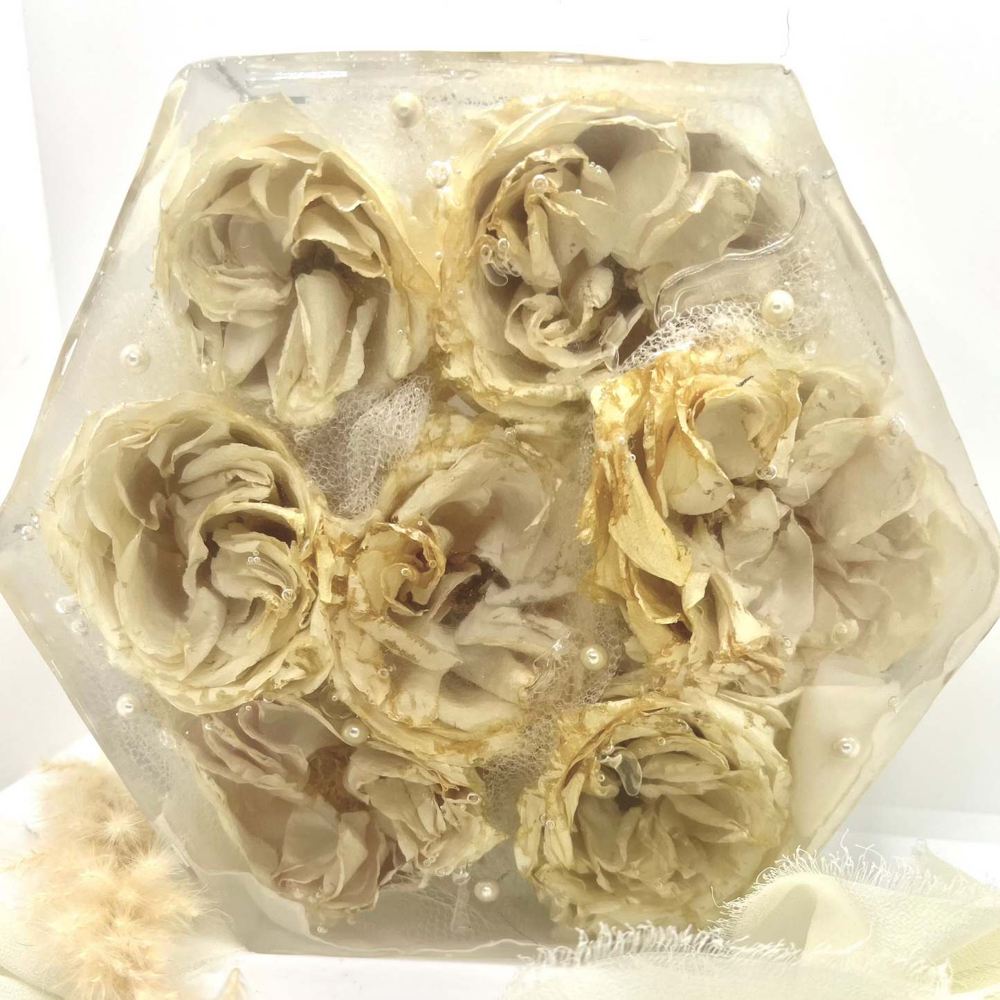 A crystal clear resin hexagon filled with white roses and white lace . A beautiful way to preserve a bridal bouquet.