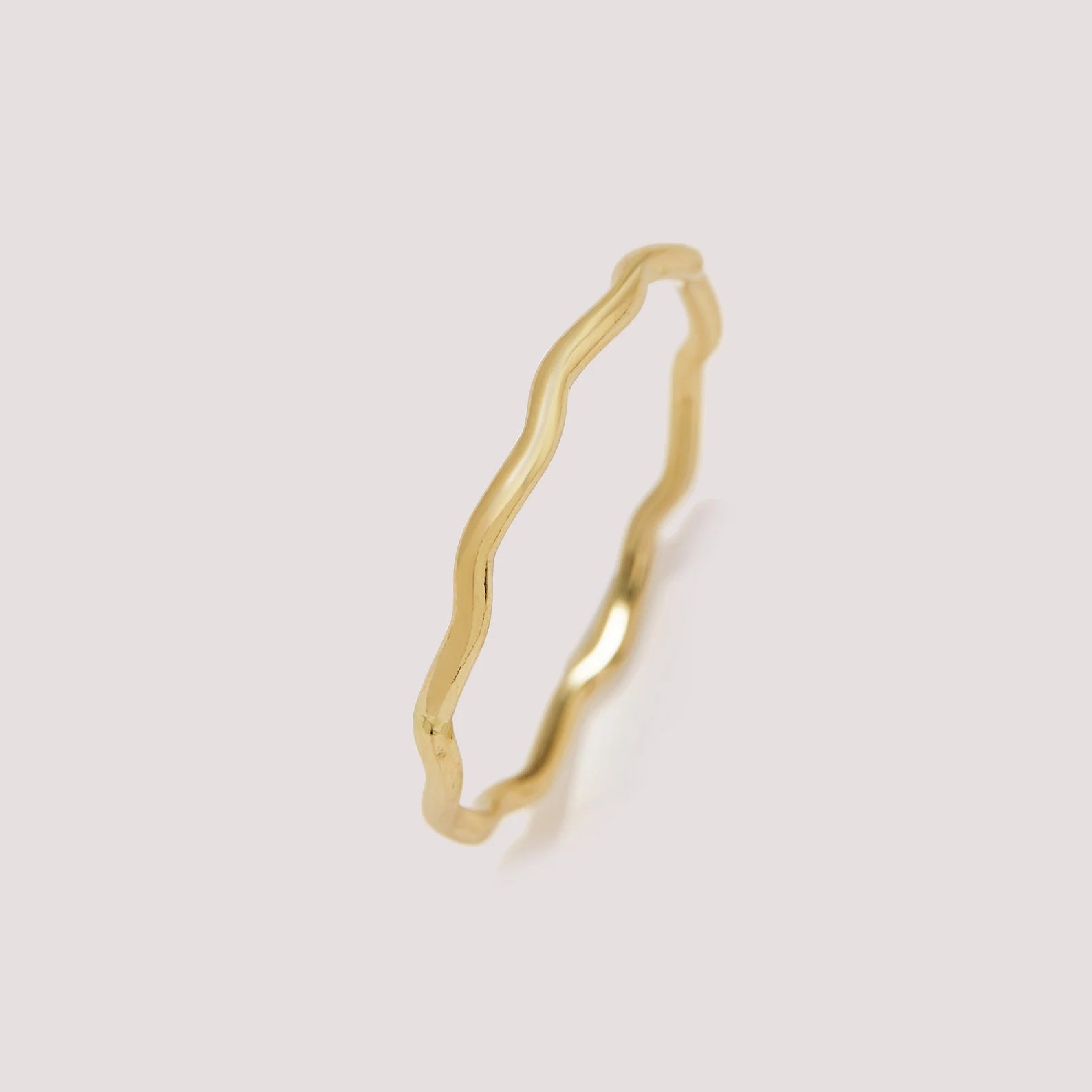 Gold ring with a wavy design on a light gray background