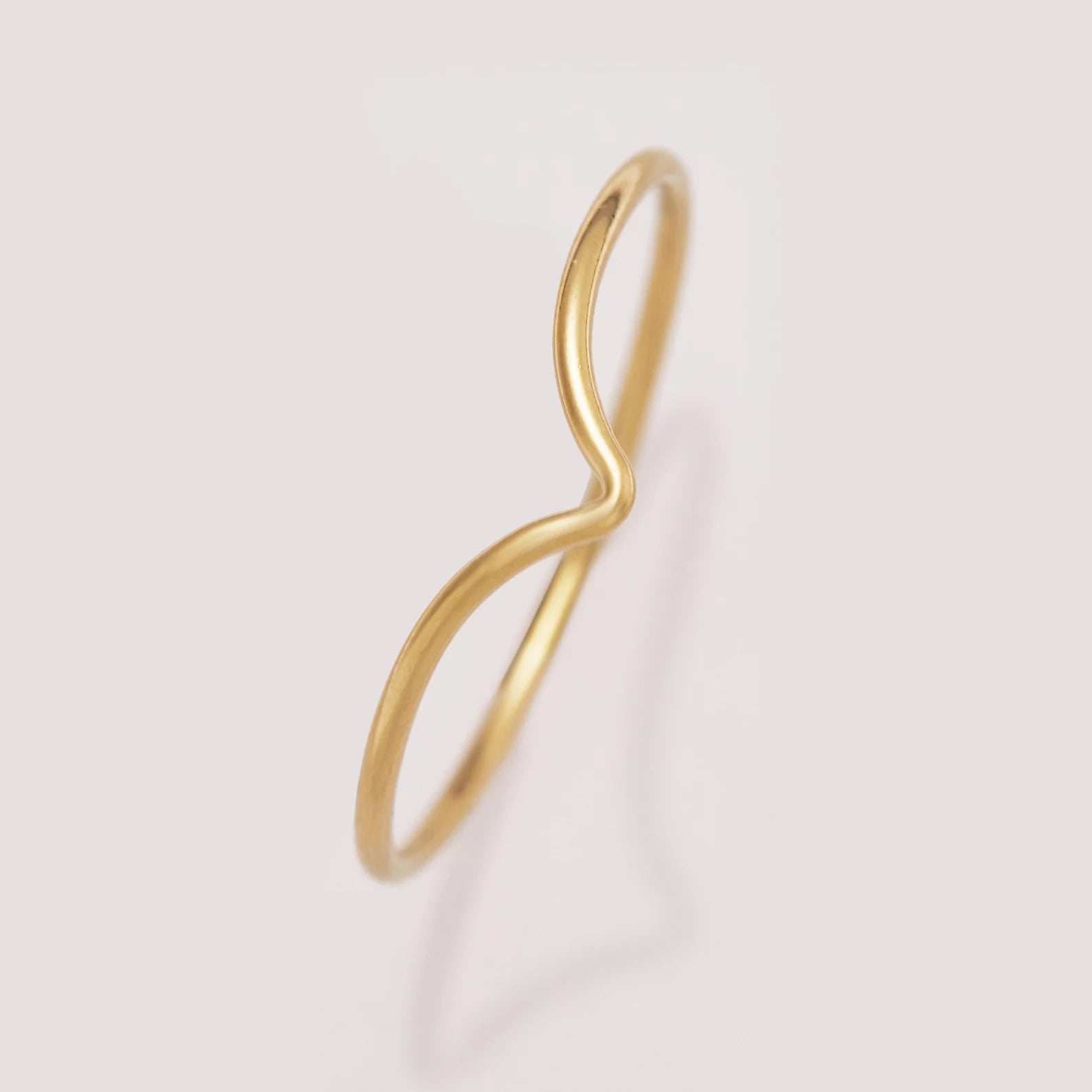 Gold infinity ring on a light pink background