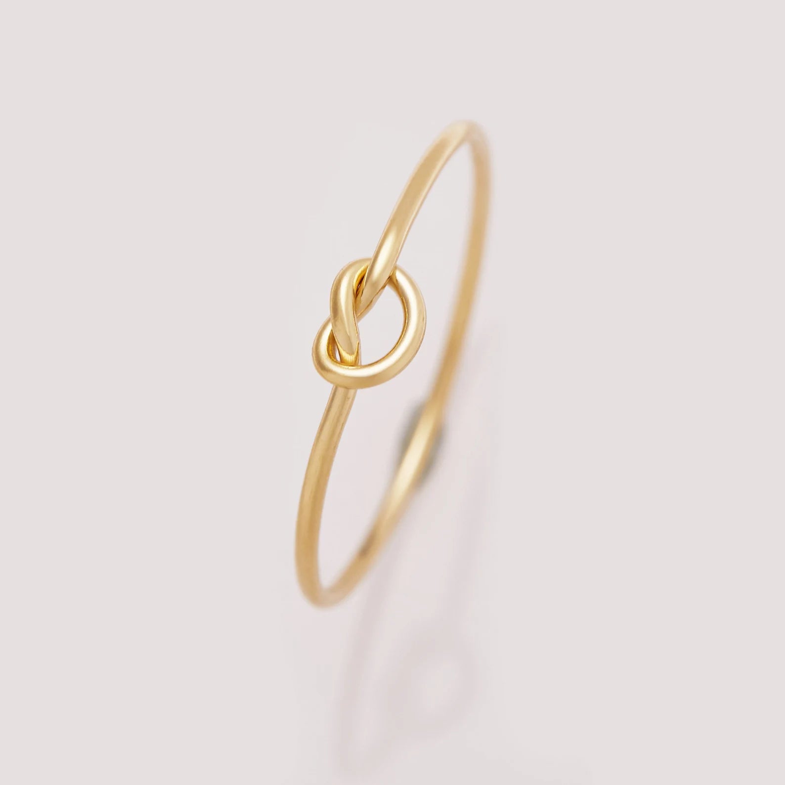 Gold ring with a knot design on a light gray background