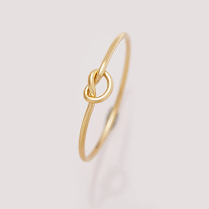 Gold ring with a knot design on a light gray background