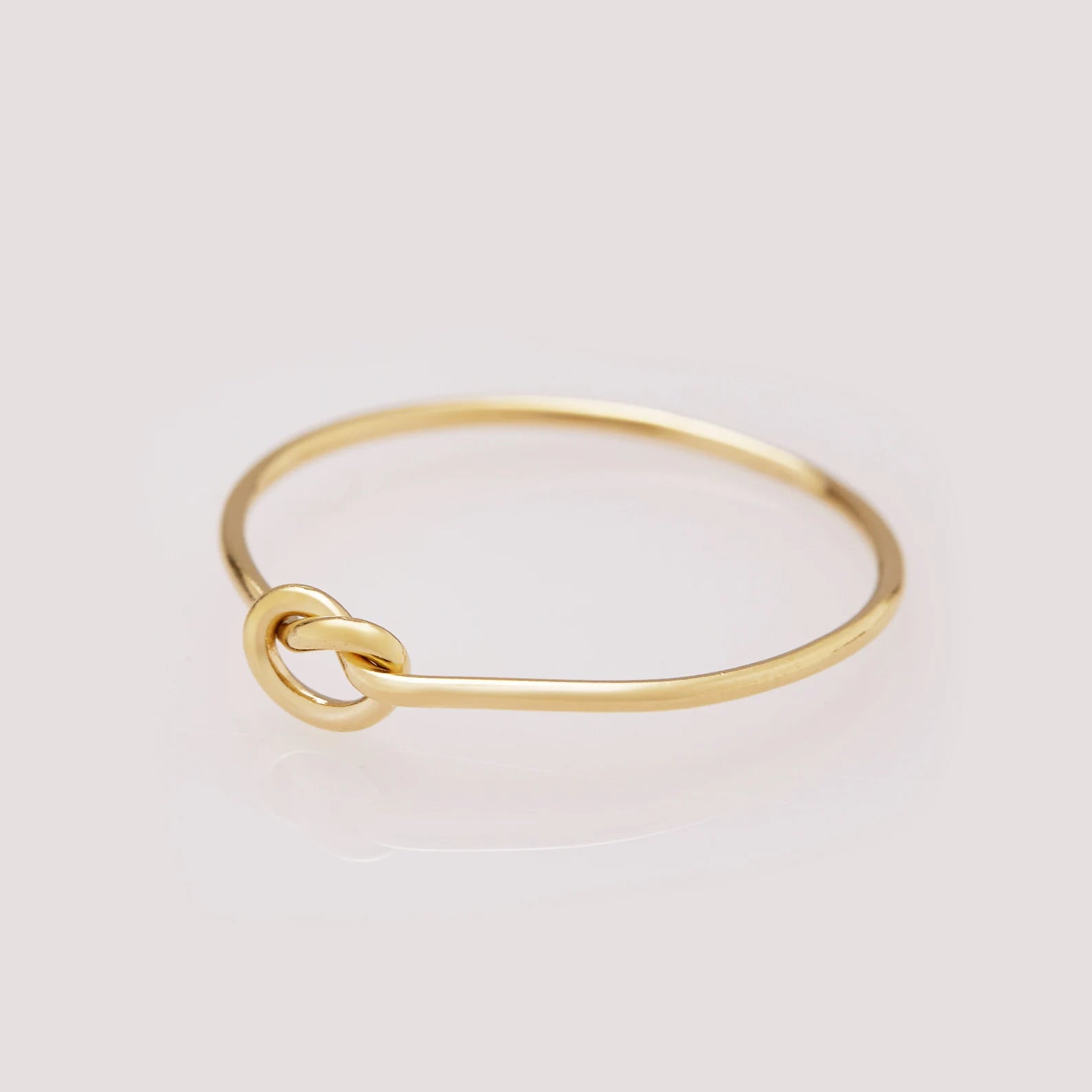 Gold ring with a knot design on a light gray background