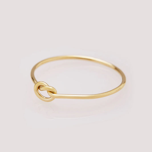 Gold ring with a knot design on a light gray background
