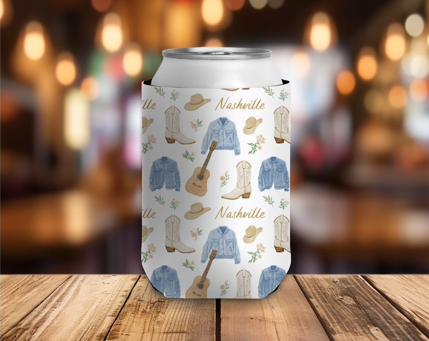 Can cooler with Nashville-themed design featuring boots, hats, and guitars on a wooden surface.