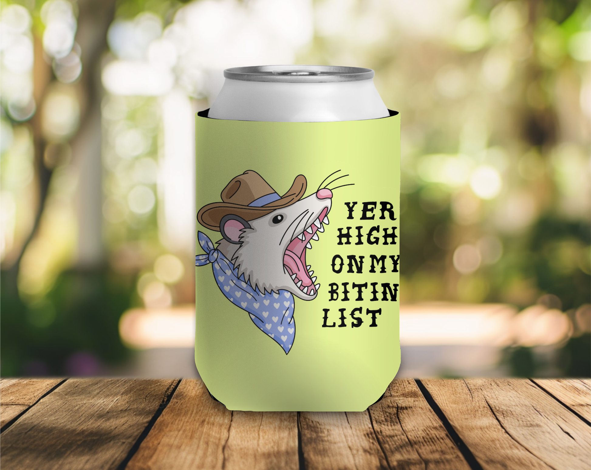 Can cooler with a cartoon mouse wearing a cowboy hat and bandana, text 'Yer High On My Bitin List' on a wooden surface with a blurred natural background.