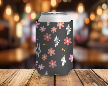 Black can cooler with floral and skeleton hand design on a wooden table with a blurred bar background