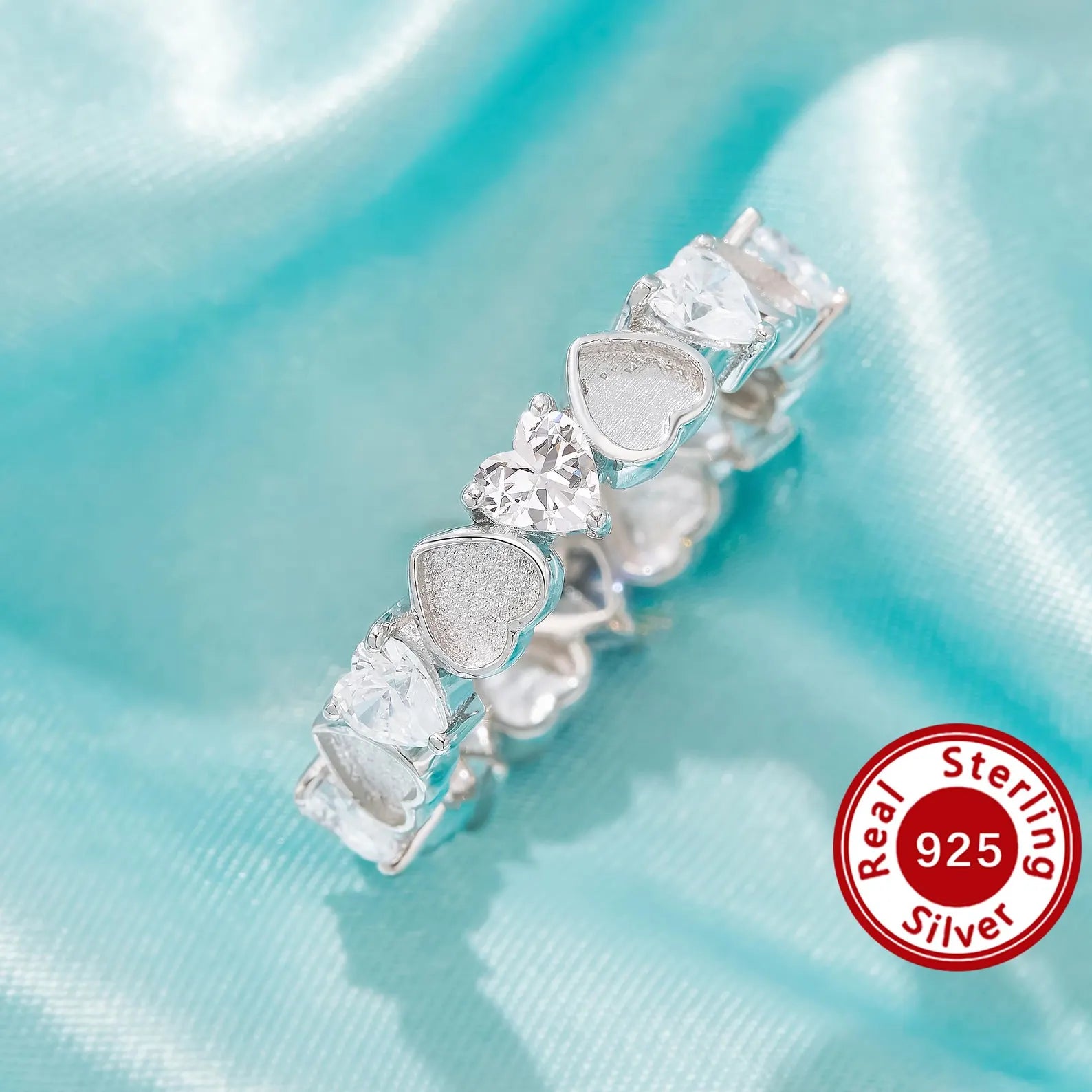 Silver earring with heart-shaped gemstones on a light blue satin background, featuring a 'Real Sterling Silver 925' stamp.