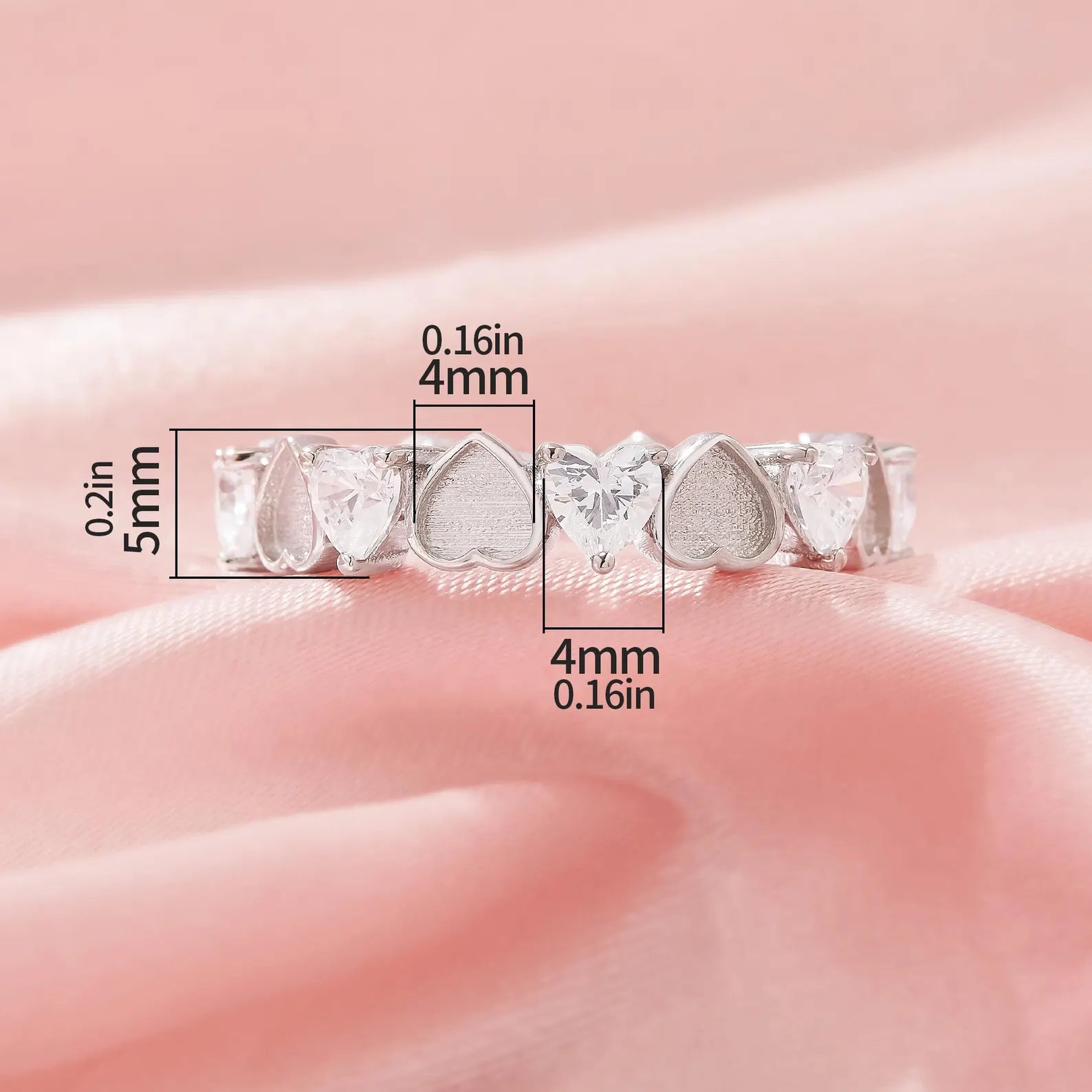 Silver ring with heart-shaped stones on a pink background, showing measurements.