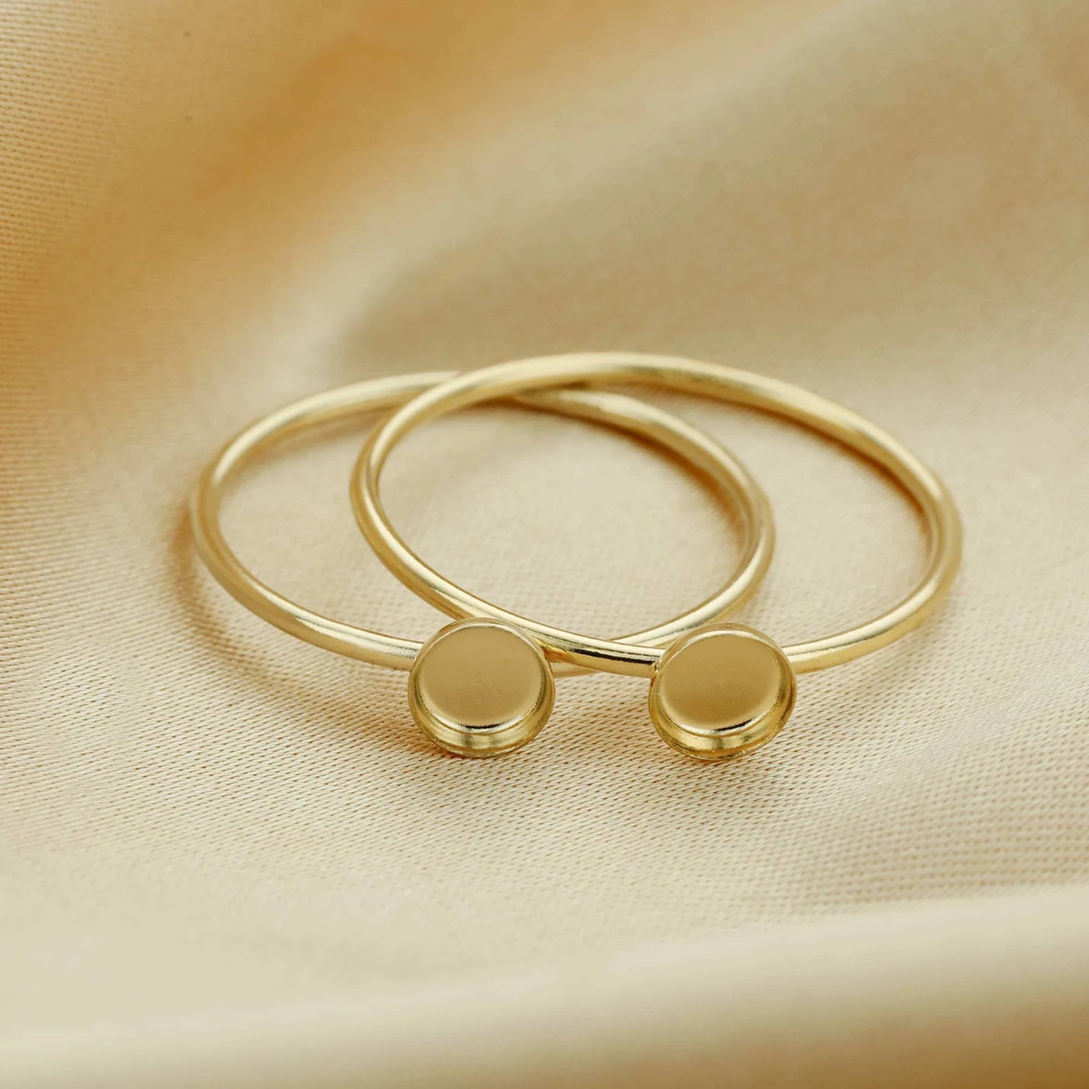 Gold bangles with round embellishments on a beige fabric background