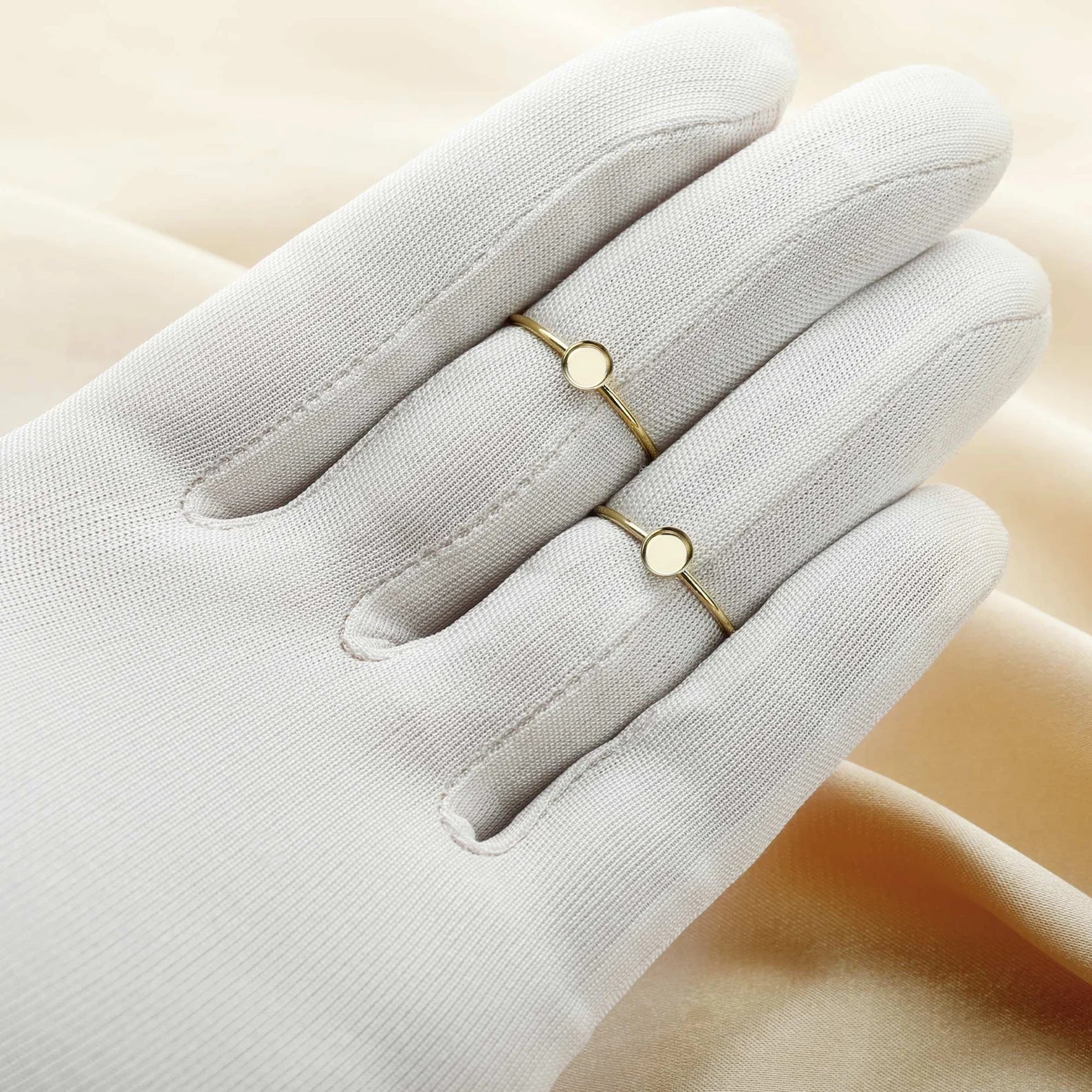 Gold ring with small round stones on a white glove against a beige background