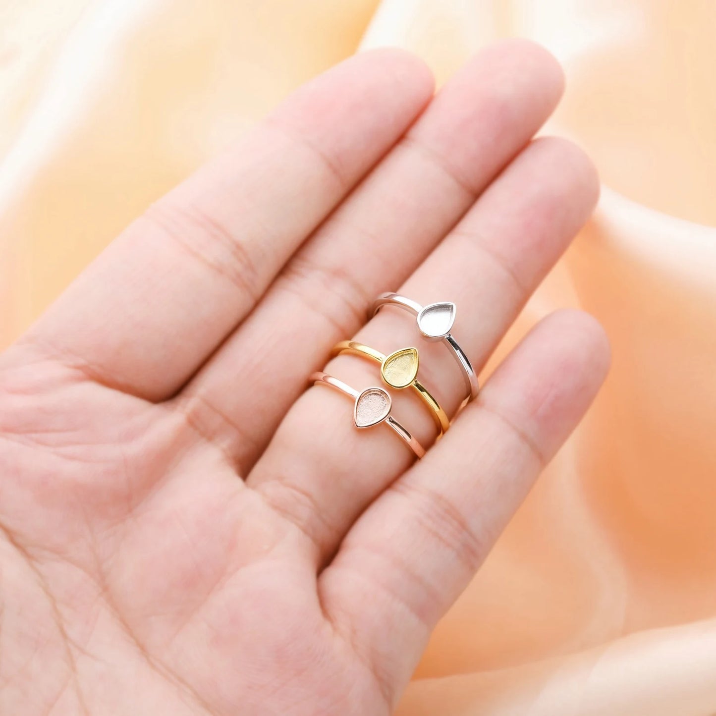 Three heart-shaped rings on a hand against a soft peach background