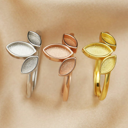 Three leaf-shaped rings in silver, rose gold, and gold on a beige background