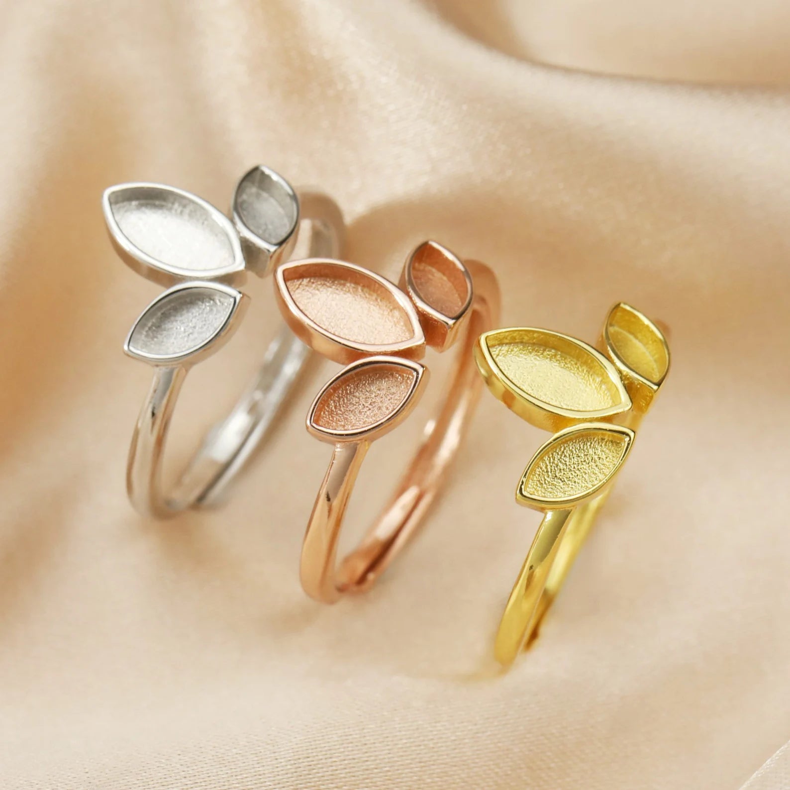 Three leaf-shaped rings in silver, rose gold, and gold on a beige background