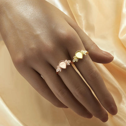 Hand wearing a gold ring with floral design on a soft peach fabric background