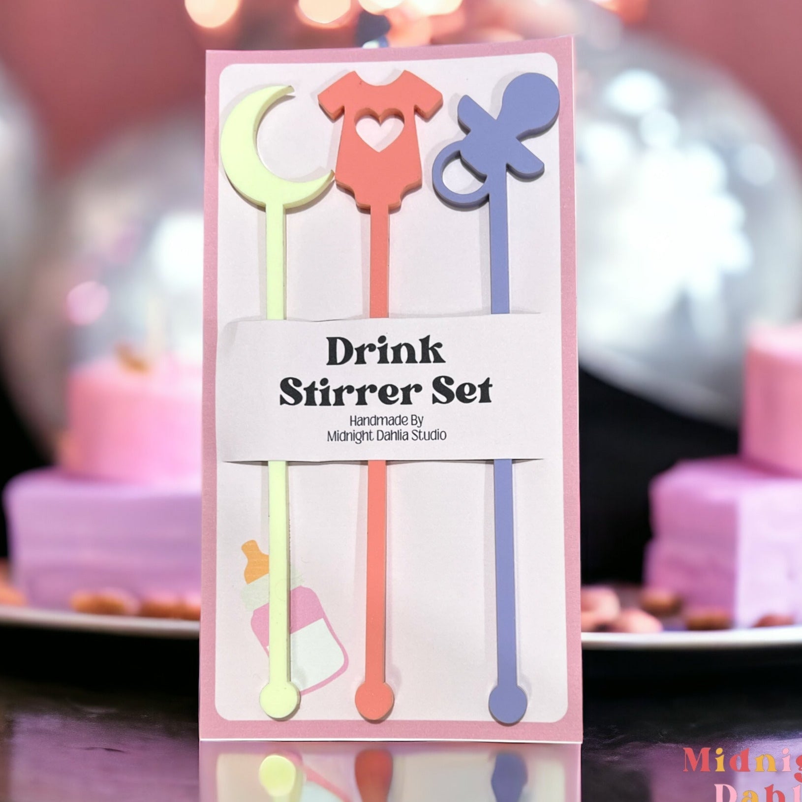 set of three drink stirrers with the top in the shape of a moon, a onesie, and a pacifier in pale light yellow, coral pink, and lavender purple.
