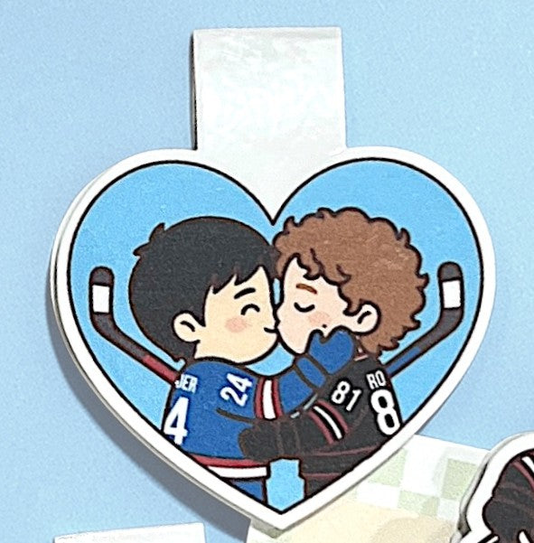Heart-shaped clip with cartoon illustration of two people embracing, on a light blue background.